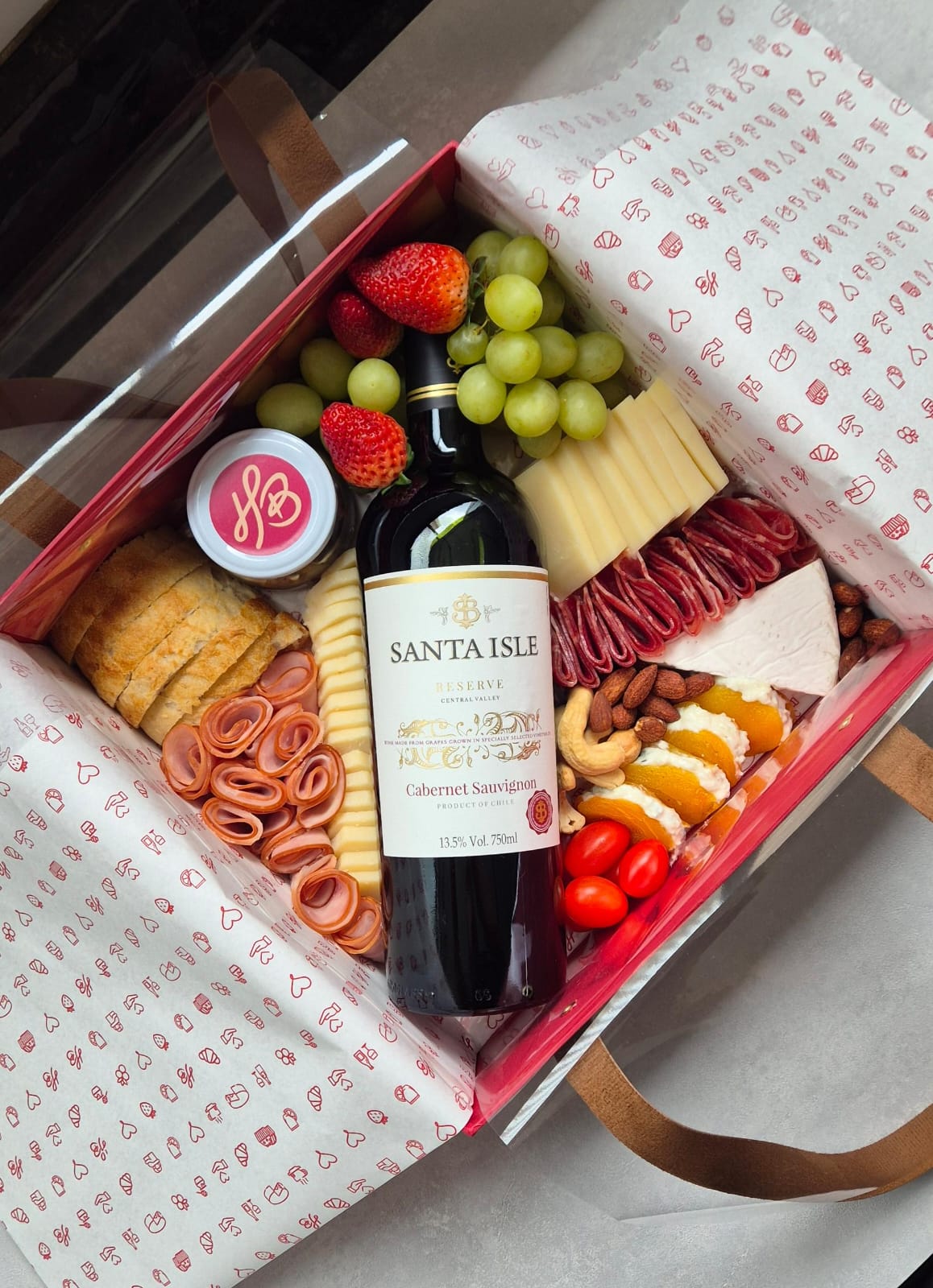 Caixa de presente com uma garrafa de vinho, taças e chocolates.